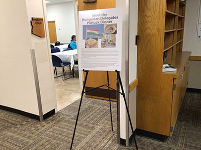 sign for Meet the Hungarian Delegates Potluck Dinner event on easel in front of entrance to Prescott Room
